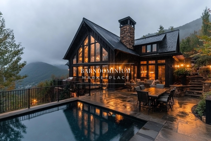 A cozy yet luxurious mountain retreat with dark wood exterior, large A-frame windows, and a glowing interior, featuring an elegant poolside patio overlooking misty mountain views.