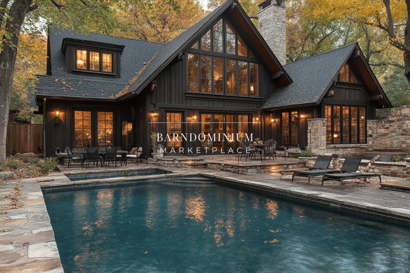 A beautifully designed black barndominium with a stone-accented pool, warm lighting, and a cozy outdoor living space, surrounded by autumn trees.