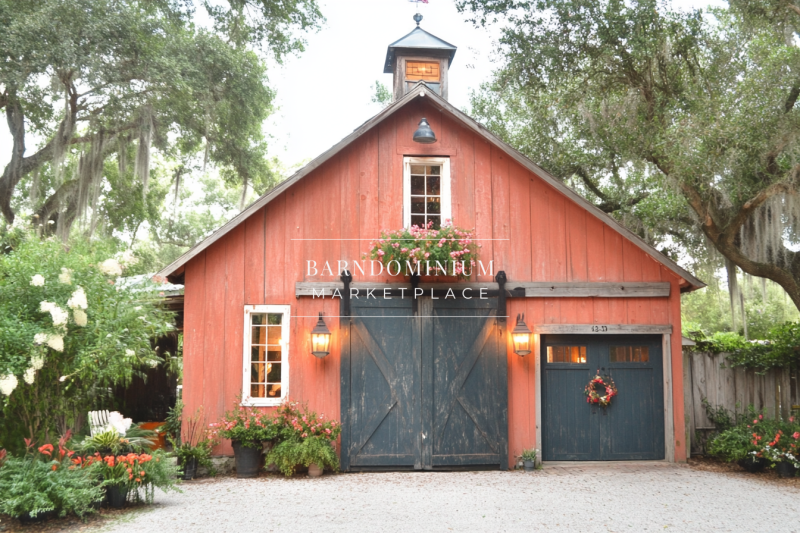 A beautifully designed rustic barndominium with warm-toned wood, charming black barn doors, and lush greenery surrounding the exterior.