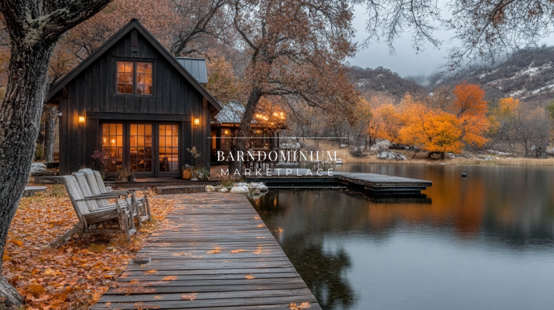 A stunning black barndominium exterior with warm glowing lights, nestled lakeside among golden autumn trees.