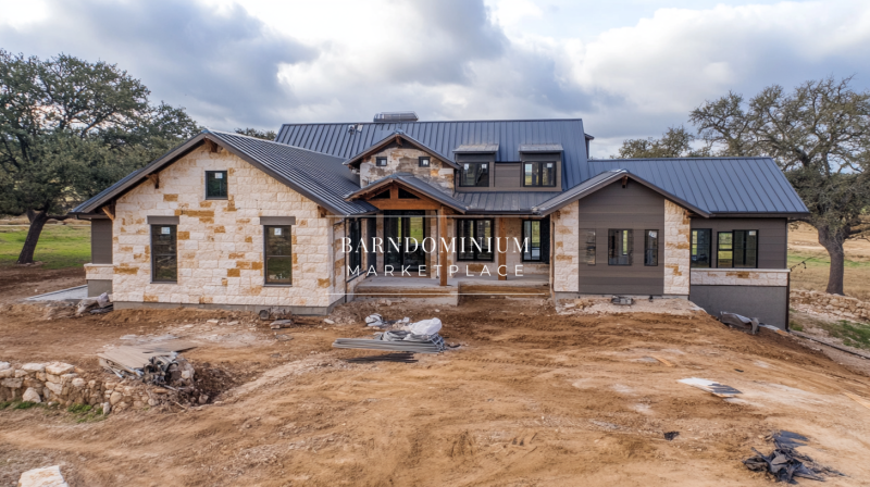 Modern barndominium under construction featuring a mix of stone and metal siding, a sleek black roof, and large windows.