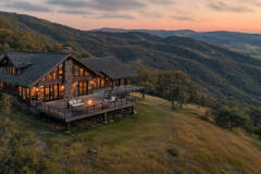 A stunning mountain barndominium with a stone and wood exterior, panoramic views, and a cozy outdoor firepit.