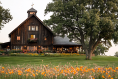 Rustic wooden barn-style home surrounded by lush greenery and wildflowers.