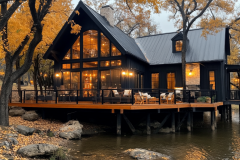 Cozy black barndominium with a waterfront deck, surrounded by autumn foliage.