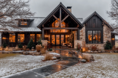 A stunning rustic barndominium with a modern farmhouse design, featuring a grand entrance, warm lighting, and a light dusting of snow for a cozy winter feel.