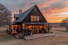 A stunning rustic barndominium with warm glowing lights, set against a breathtaking sunset over the open countryside.