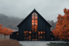 A sleek black barndominium with a striking glass front, glowing warmly against a misty autumn backdrop, creating a modern yet rustic charm.