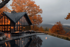 Modern glass-walled barndominium overlooking a stunning autumn landscape, with a sleek infinity pool reflecting the warm glow of the home’s interior.