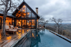 A stunning modern barndominium with an infinity pool, floor-to-ceiling windows, and warm interior lighting, offering breathtaking hillside views.
