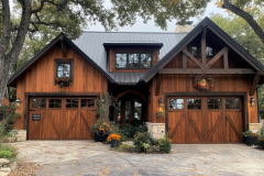 Charming rustic barndominium with rich wooden tones, large garage doors, and warm autumn décor, nestled among towering oak trees.