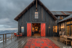 Stylish black barndominium with bold red barn doors, a cozy outdoor deck, and breathtaking mountain views, creating the perfect modern rustic retreat.