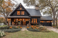 A modern black barndominium with warm lighting, rustic charm, and beautifully landscaped surroundings, creating the perfect cozy retreat.