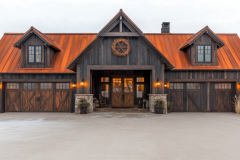 Modern black barndominium with a striking copper roof, wooden accents, and warm exterior lighting.