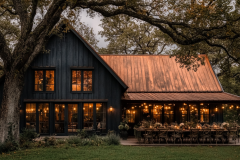 Elegant black barndominium with a copper roof, warm glowing lights, and an enchanting outdoor dining setup.