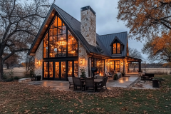Stunning barndominium exterior with a modern rustic design, featuring a grand stone chimney, floor-to-ceiling windows, and warm ambient lighting.