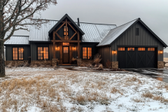 A modern black farmhouse with rustic wood accents, glowing windows, and a light dusting of snow, creating a cozy winter ambiance.