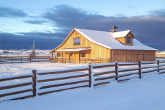 A picturesque wooden barndominium bathed in golden sunlight, standing gracefully amid a pristine, snow-covered landscape.