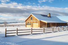 A picturesque wooden barndominium surrounded by pristine snow, reflecting the beauty of rural winter living.