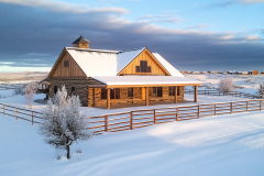 A stunning rustic barndominium nestled in a serene, snow-covered landscape, illuminated by golden sunlight.
