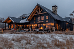 Rustic barndominium with a cozy winter ambiance, featuring a black metal roof, wooden beams, and warm interior lighting.