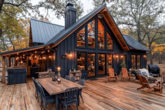 Rustic black barndominium with floor-to-ceiling windows, warm lighting, and a spacious wooden deck.