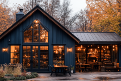 Modern black barndominium with warm interior lighting, large glass windows, and a cozy autumn atmosphere.