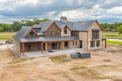 A luxurious barndominium-style home under construction, featuring a blend of rustic wood and stone exterior with a sleek metal roof.