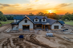 A gorgeous barndominium under construction, set against a stunning sunset, blending modern farmhouse and rustic charm.