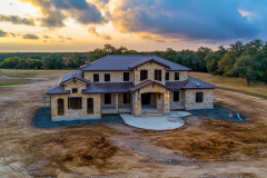 A stunning barndominium with rustic stone exterior and a modern metal roof, set against a breathtaking sunset.