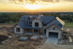 A stunning stone-clad barndominium under construction, set against a breathtaking sunset view.