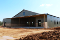 A spacious green barndominium with a covered porch, blending rustic charm with modern metal construction.