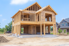 A two-story barndominium under construction, showcasing its wooden framing and open layout, set in a developing neighborhood.
