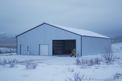 A steel barndominium in a snowy landscape, featuring a large open garage and a simple yet durable design.