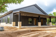 A stylish black barndominium featuring a spacious covered porch with stone-accented columns, blending modern design with rustic charm.