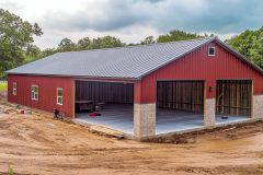 A spacious red barndominium with a durable metal roof and stone-accented base, offering a blend of functionality and rustic charm.