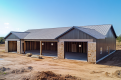 A newly constructed barndominium with a modern metal exterior and stone accents, featuring open garage bays for a spacious layout.