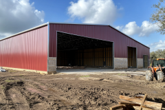 A large red metal barndominium under construction, featuring a wide-open entrance and a durable steel frame.