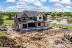 Gorgeous two-story barndominium under construction, set in a scenic rural landscape with a pond view.