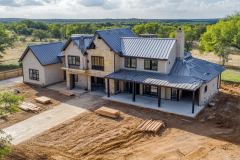 Elegant two-story barndominium with a modern farmhouse design, featuring a covered porch and black metal roofing.