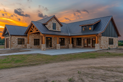 Beautiful rustic barndominium exterior with stone and wood accents, set against a stunning sunset backdrop.