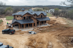 Barndominium under construction on a rural property, featuring a modern rustic design with a black metal roof and wooden exterior.