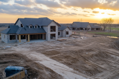 Spacious barndominium under construction with a modern farmhouse design, large open land, and a beautiful sunset backdrop.