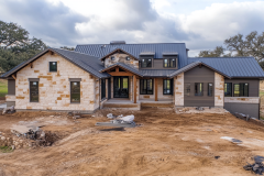 Modern barndominium under construction featuring a mix of stone and metal siding, a sleek black roof, and large windows.