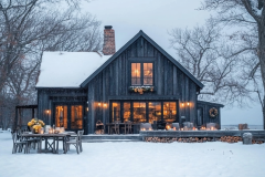 Charming black barndominium in a serene winter setting, warmly lit with rustic holiday décor and a cozy outdoor dining space.