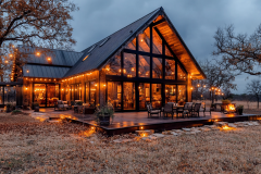 Stunning modern barndominium with floor-to-ceiling windows, warm string lights, and a cozy outdoor patio.