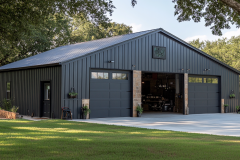 Spacious black barndominium with large garage doors, a sleek metal roof, and an open workspace, nestled in a green landscape.