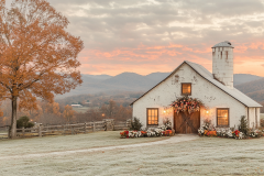 Elegant white barndominium exterior with rustic charm, adorned with floral decor, set against a breathtaking mountain sunrise.
