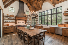 Rustic barndominium kitchen with exposed wood beams, farmhouse-style cabinetry, and a large wooden dining table.