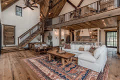 Spacious barndominium living area with vaulted ceilings, exposed wooden beams, and an open loft, combining rustic charm with modern elegance.