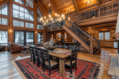 Luxurious barndominium interior with a grand dining area, rustic log walls, a striking chandelier, and a lofted second-floor balcony overlooking the space.